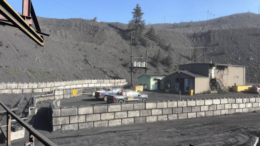Robust Engineering pickup truck parked among industrial mass-block walls at a heavy-industry coal handling site, with spoil heap and operations buildings in the background