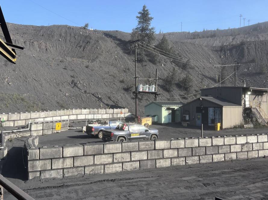 Robust Engineering pickup truck parked among industrial mass-block walls at a heavy-industry coal handling site, with spoil heap and operations buildings in the background