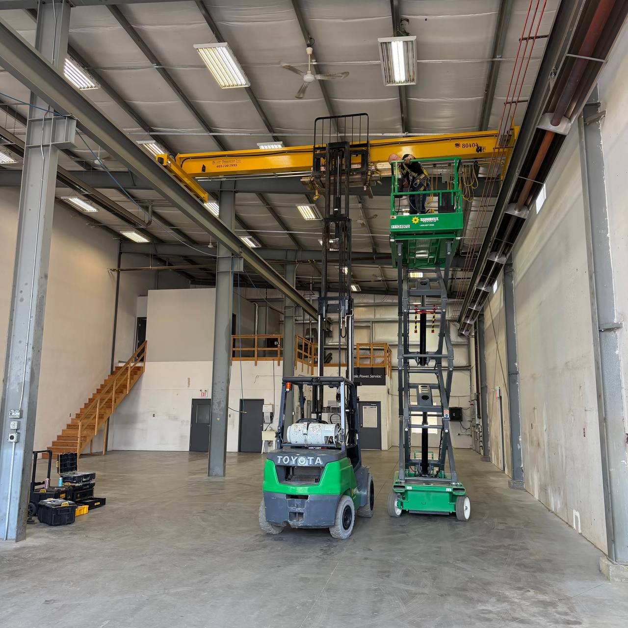 Worker on scissor lift accessing 5-ton overhead crane in industrial facility