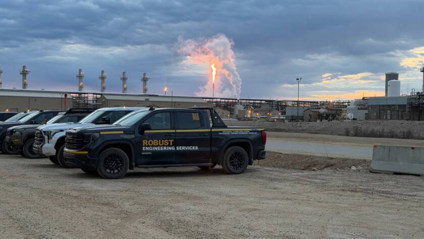 Black Robust Engineering Services pickup truck parked at industrial site with flare stack and pipes at Cenovus Christina Lake during monorail commissioning