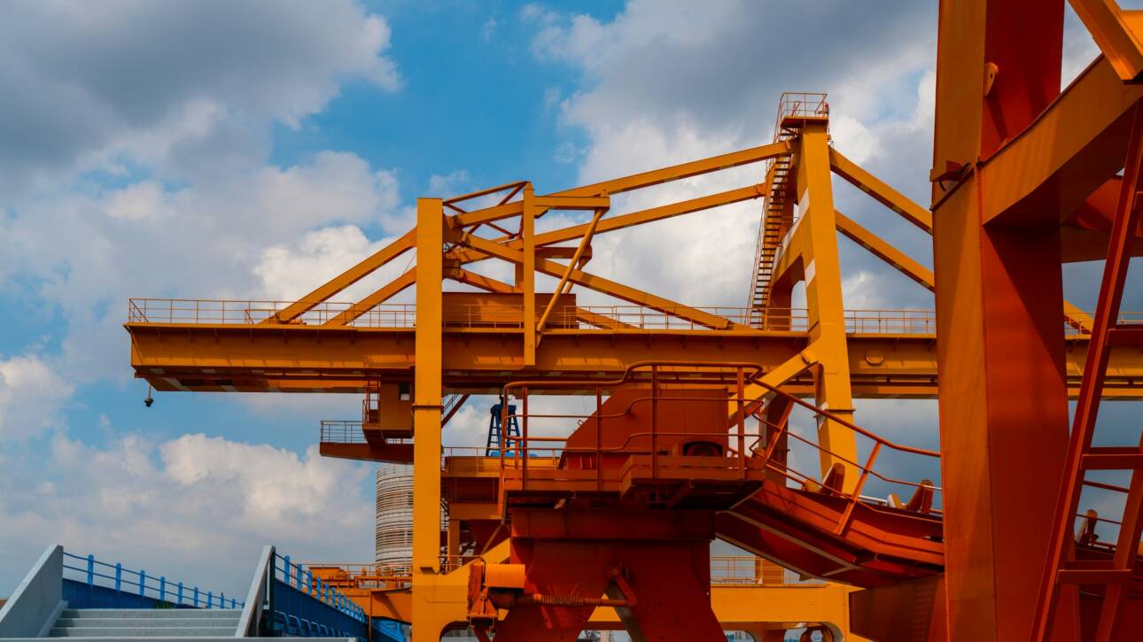 Large orange industrial overhead cranes against a cloudy blue sky